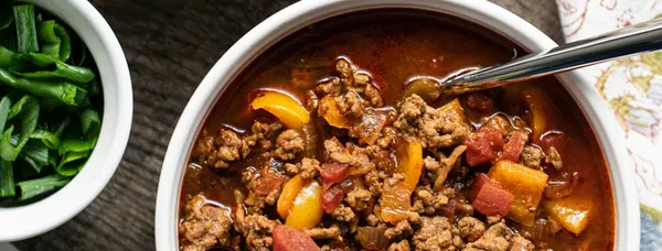 Herzhafte Hackfleisch-Gemüsesuppe in der Schale, daneben Frühlingszwiebeln